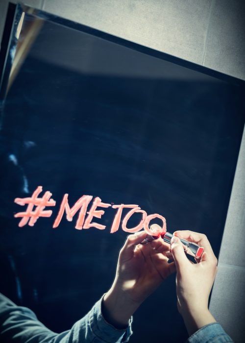 Girl writing "#metoo" on a mirror with a red lipstick.