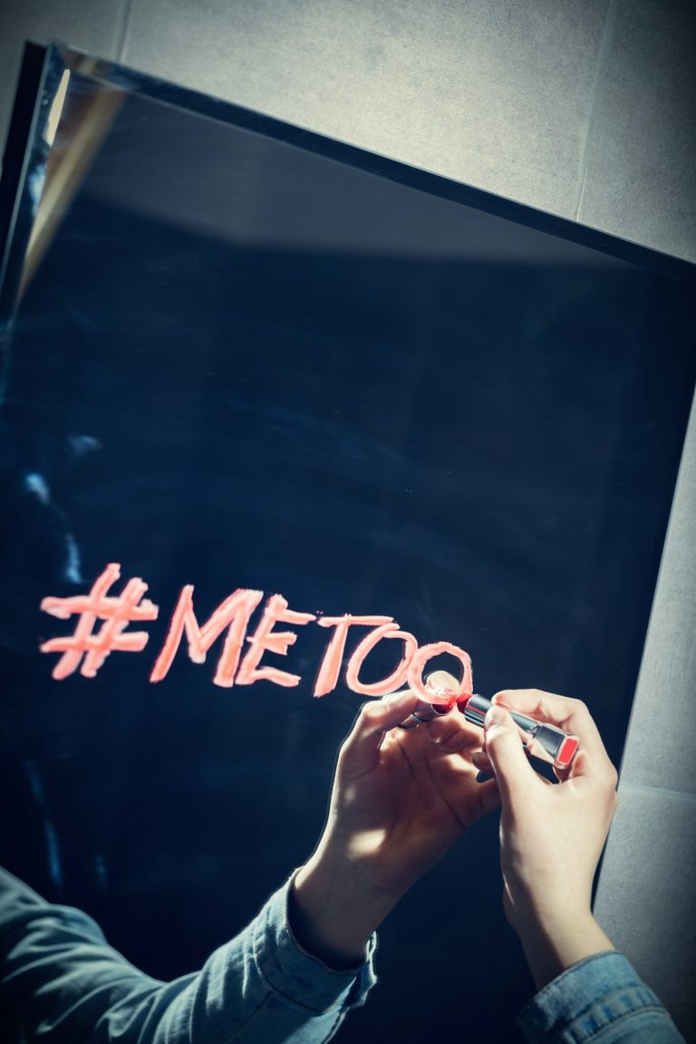 Girl writing "#metoo" on a mirror with a red lipstick.